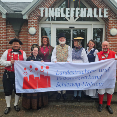 Sieben Personen mit Banner "Landestrachten- und Volkstanzverband Schleswig-Holstein"