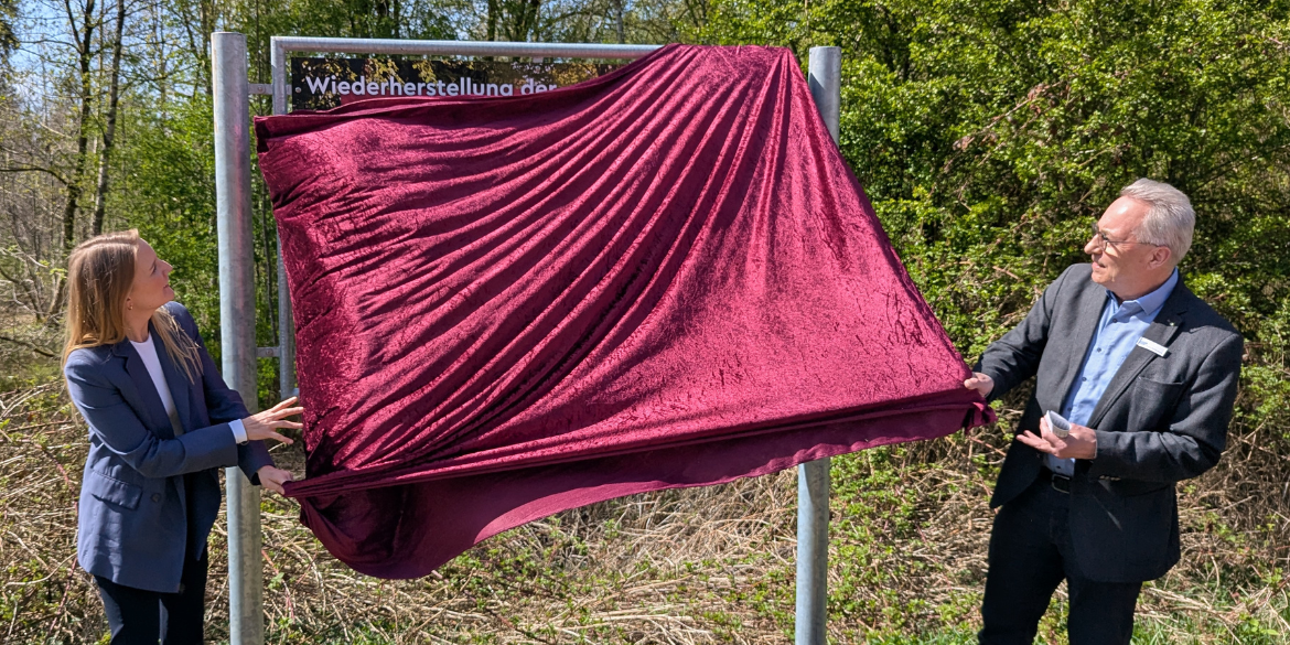 Zwei Personen ziehen Tuch von Schild