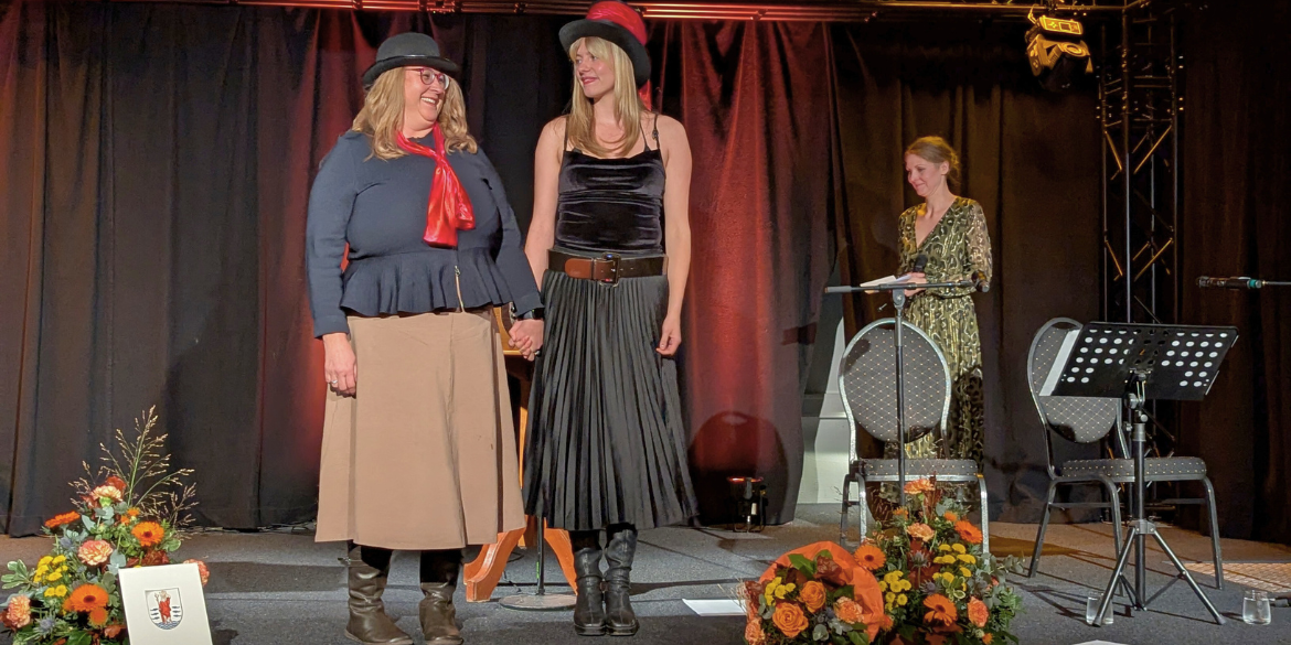 Zwei Personen verbeugen sich auf Bühne, eine Person im Hintergrund