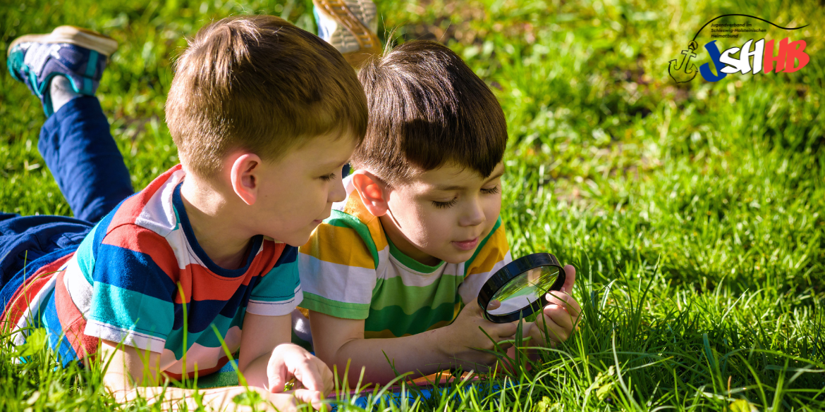 Zwei Jungs liegen auf einer Wiese und untersuchen etwas mit einer Lupe © Pahis Getty Images