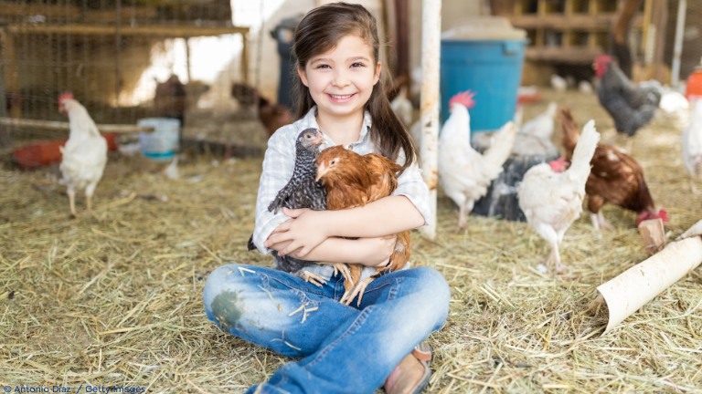 Kind in Hühnerhof mit zwei Hühnern auf dem Schoß