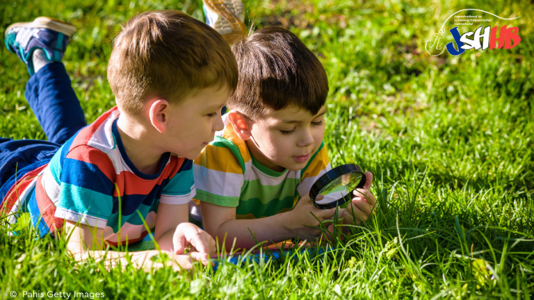 Zwei Jungs liegen auf einer Wiese und untersuchen etwas mit einer Lupe