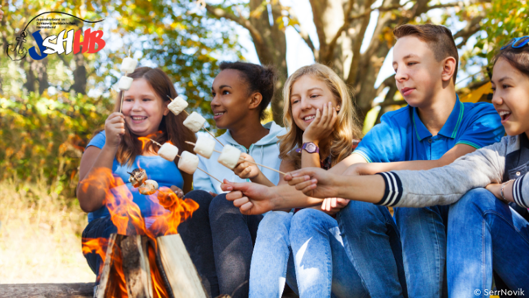 Jugendliche sitzen am Lagerfeuer und rösten Marshmallows